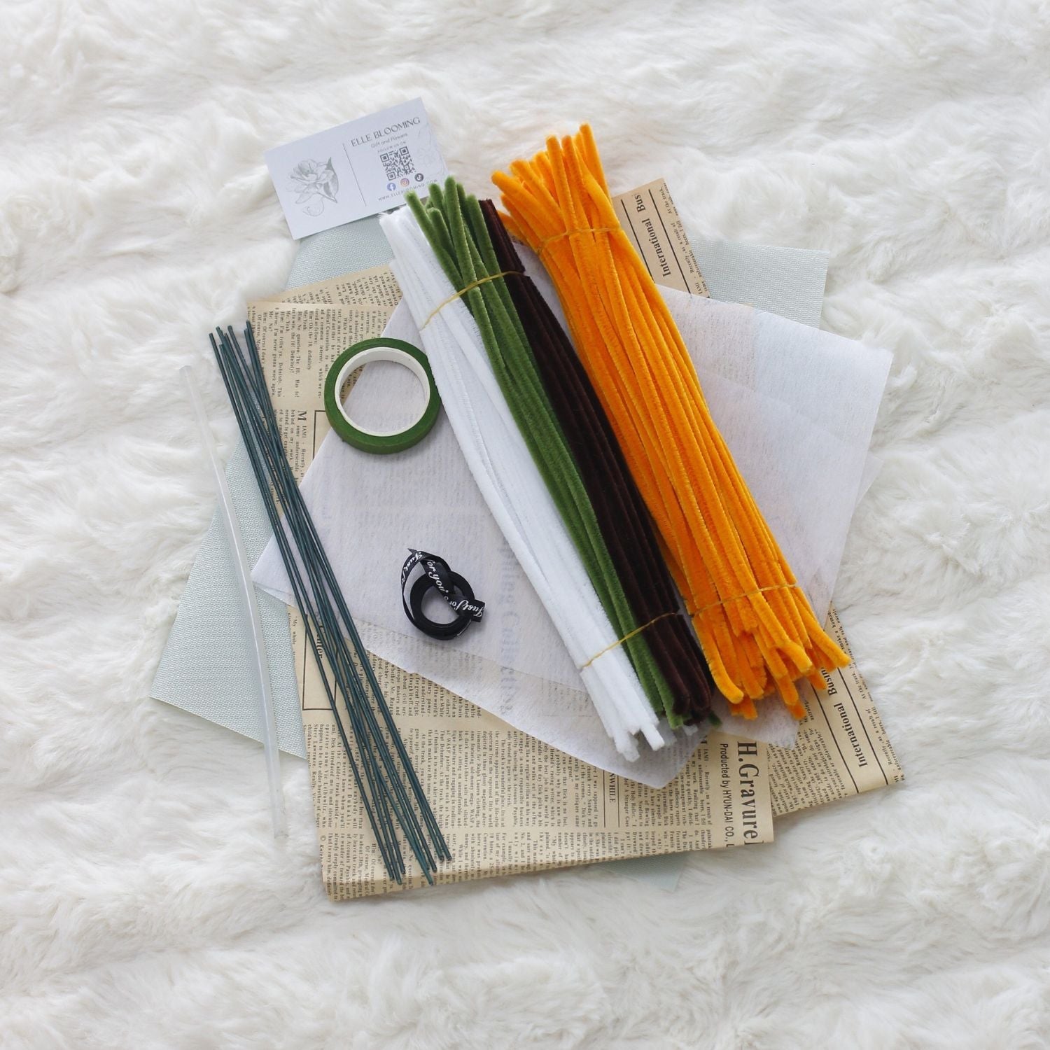 DIY bouquet of vibrant orange sunflowers and small white daisies made from fuzzy pipe cleaners. Wrapped in vintage-style kraft and pastel paper with a black ribbon perfect for handmade gift lovers.