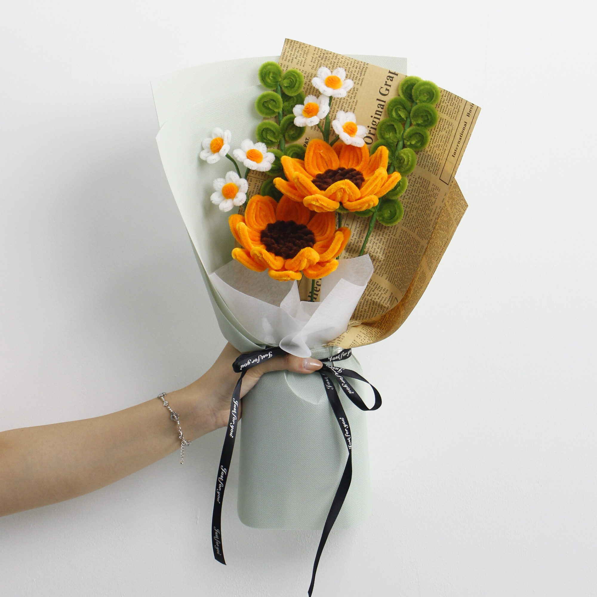 DIY bouquet of vibrant orange sunflowers and small white daisies made from fuzzy pipe cleaners. Wrapped in vintage-style kraft and pastel paper with a black ribbon perfect for handmade gift lovers.