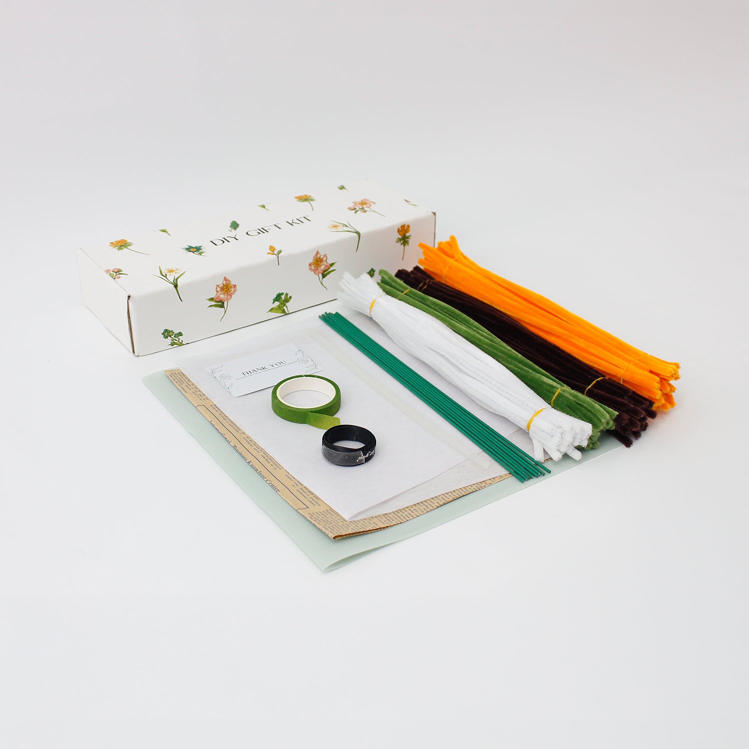 DIY bouquet of vibrant orange sunflowers and small white daisies made from fuzzy pipe cleaners. Wrapped in vintage-style kraft and pastel paper with a black ribbon perfect for handmade gift lovers.