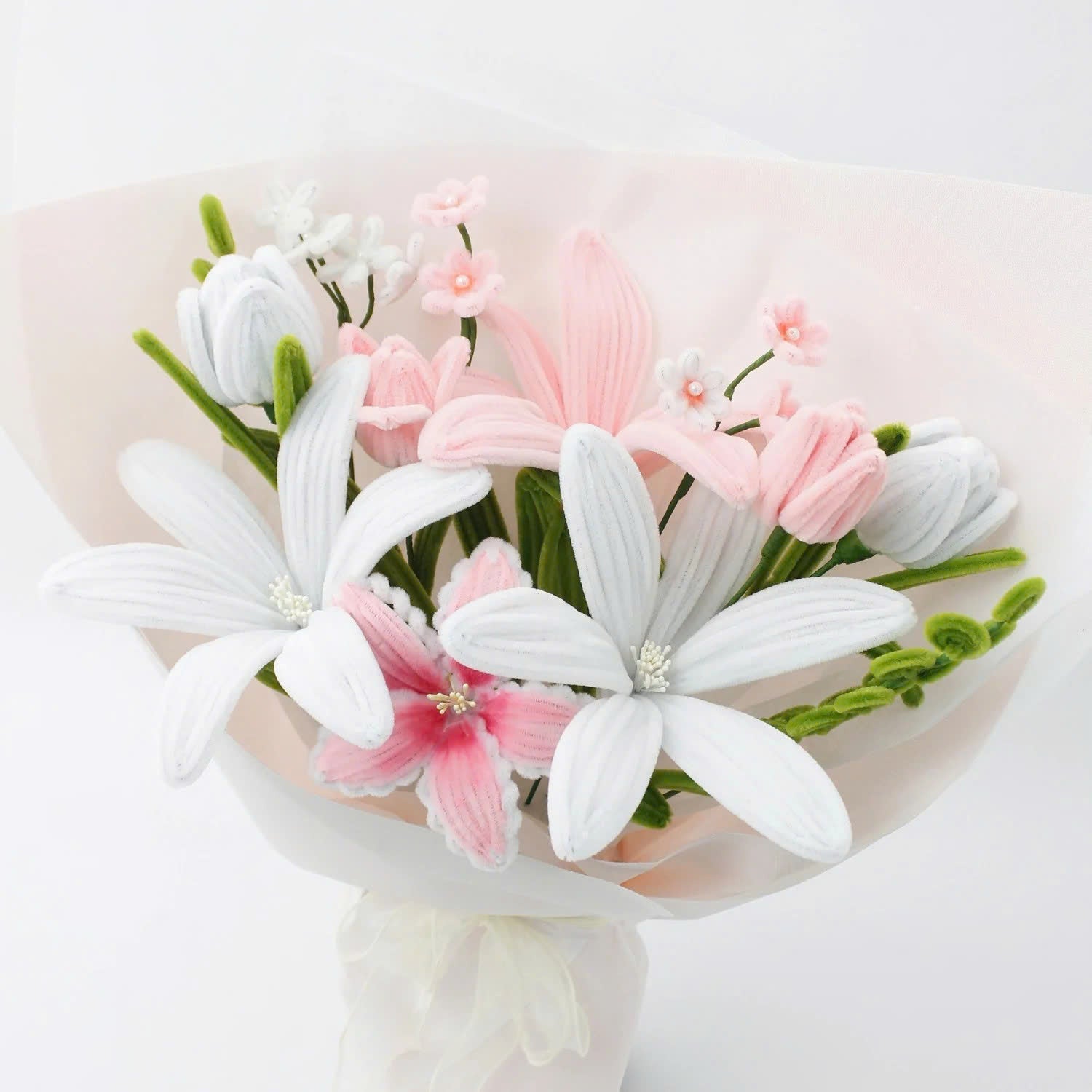 Pastel Bloom DIY bouquet crafted from pipe cleaners, featuring soft white and blush pink lilies, tulips, and delicate filler flowers. Wrapped in sheer pastel wrapping with a flowing organza ribbon an elegant, handmade floral craft kit for gifting or display.